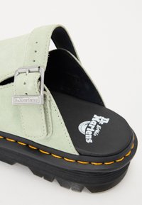 Világos zöld velúr szandál széles felső pánttal, ezüst csattal és Dr. Martens logós feketén párnázott talpbetéttel. Vastag fekete talp sárga varrással.