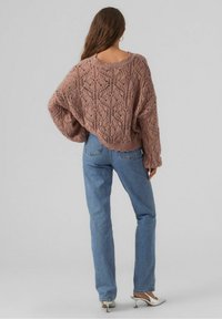 Raita-kudottu, mauve-värinen neuletakki, jossa on löysä istuvuus ja oversized-hihat. Yhdistetty vaaleansinisiin farkkuihin ja valkoisiin korkokenkiin.