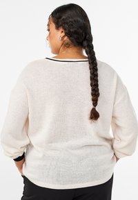 Gaiši bēšs adīts džemperis ar brīvu piegriezumu, platiem piedurknēm un melnu akcentu ap kakla izgriezumu. Faktūru audums, daļēji caurspīdīgs.