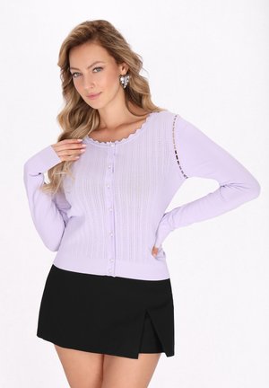 Lilac cardigan with ribbed texture, round scalloped neckline, button front, and long sleeves. Paired with a short black skirt.