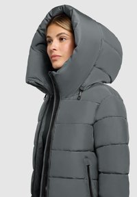 Grå polstret jakke med en stor, rund hætte, frontlynlås og sidelommer. Glat tekstur med quiltet design til isolering.