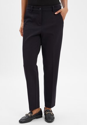 Marineblaue, maßgeschneiderte Hose mit geradem Bein, ausgestattet mit Fronttaschen, einem Knopfverschluss und einem glatten Stofftextur. Gezeigte schwarze Slipper.