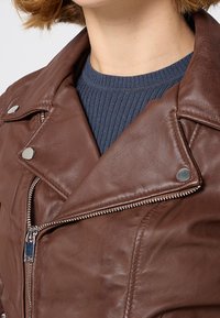 Brązowa skórzana kurtka motocyklowa z metalowymi akcentami, z zamkiem błyskawicznym i zatrzaskami. Posiada lekko teksturowaną powierzchnię oraz wyłogi.