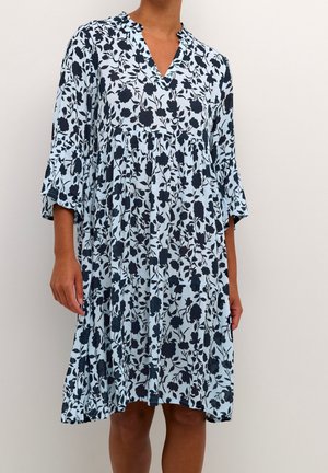 Loose, knee-length dress with three-quarter sleeves, light blue fabric featuring a black floral pattern, worn by a standing person.