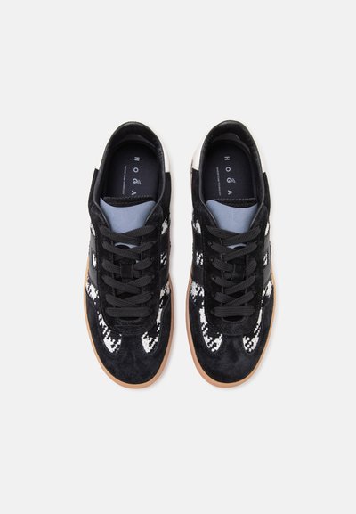 Paire de baskets noires avec des accents blancs et gris à motifs, des lacets noirs et des semelles marron clair, vues de dessus sur fond blanc.