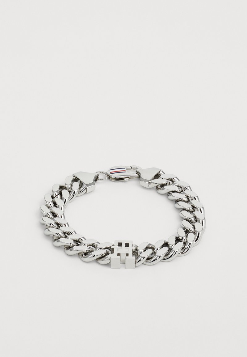 Pulseira de corrente grossa em prata com um fecho em caixa que apresenta um design em recorte da letra "H" e um fecho tipo lagosta com riscas vermelhas, brancas e azuis.