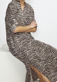 Lång, löst sittande klänning med zebramönster i beige och brunt. Har en mandarinkrage och uppvikta ärmar, med sidofickor.