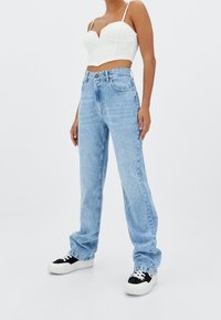 Jeans rectos de mezclilla en azul claro, con una cintura alta y diseño clásico de cinco bolsillos. Combinados con un top corto blanco y zapatillas negras.