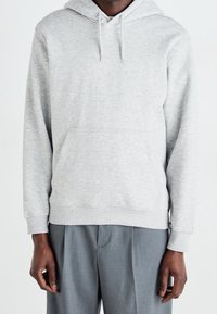 Lichtgrijze hoodie met een buidelzak, aantrekkoorden bij de capuchon, ribgebreide manchetten en zoom. Draag over een grijze broek. Zachte stofstructuur.