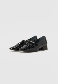 Black patent leather low-heeled shoes with a pointed toe, featuring a decorative strap and bow accent on the front.