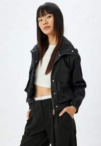 Svart kort jacka med dragkedja fram, tryckknappar och sidofickor. Har en strukturerad krage och elastiska mudgar. Matchad med högmidjade byxor.