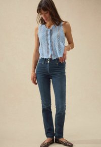 Top de tirantes de encaje azul claro con bordes en forma de punta, cierre de botones, combinado con jeans azul oscuro, con un diseño ajustado y bolsillos frontales.