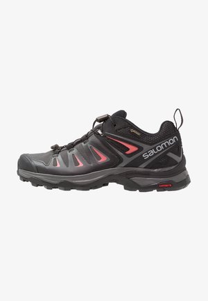 Zapatilla de senderismo Salomon negra y gris oscuro con detalles en rojo, etiqueta Gore-Tex, sistema de cordones rápidos y suela resistente con tecnología Contagrip.
