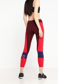 Legginsy o wysokim stanie w kolorach czerwonym, burgundowym i granatowym, ze wzorem w blokach kolorów oraz detalem z logo na dolnej części nogawki. Wykonane z elastycznego materiału.