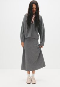 Grå strikket sweater med løs pasform og droppe skuldre, parret med en matchende lang grå nederdel. Lys pink fodtøj fuldender outfittet.