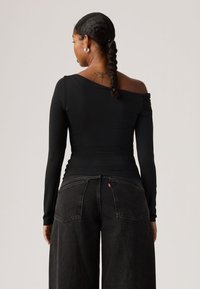 Μαύρο τοπ με μακριά μανίκια, ασύμμετρο ντεκολτέ και λεπτομέρεια με ρίγες στους ώμους, συνδυασμένο με μαύρο τζιν παντελόνι υψηλής μέσης και φαρδιάς γραμμής.