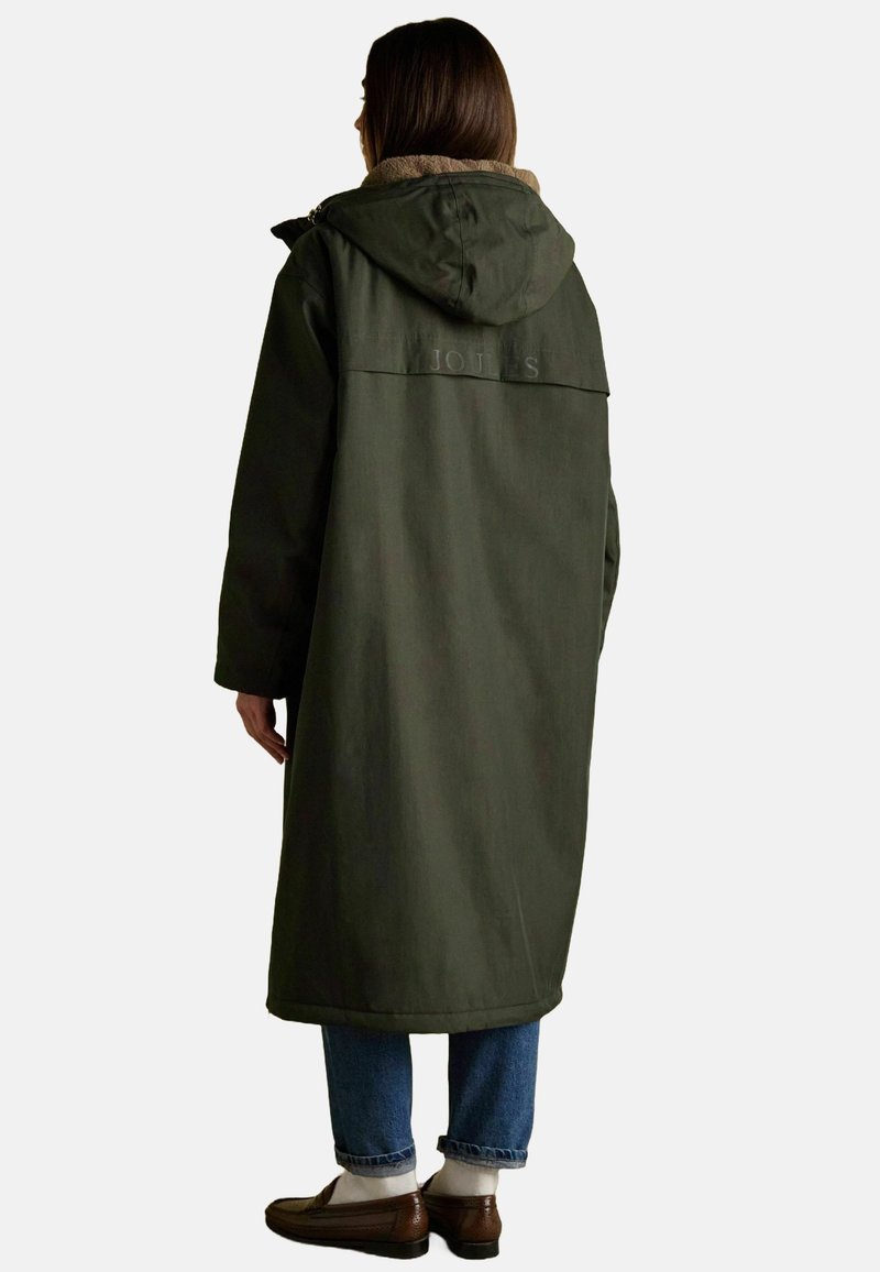 Lang grøn frakke med hætte, lavet af tekstureret stof. Har en tan indvendig foring og prægede logo på ryggen. Bæres over jeans og sko.