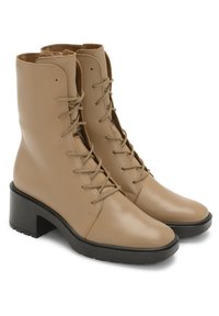 Beżowe skórzane botki sięgające do kostki z gładkim wykończeniem, sznurowanym przodem i masywnym czarnym obcasem. Posiadają okrągły nosek i teksturowaną podeszwę dla lepszej przyczepności.