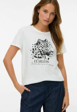 Kobieta w białej koszulce z czarną ilustracją głowy lamparta i napisem "BEZSTRACHOWA Poczuj strach i po prostu zrób to", ubrana w ciemnoniebieskie spodnie.