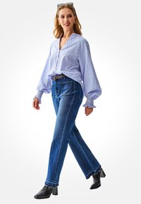 Lichtblauwe en wit gestreepte blouse met geplooide ballonmouwen, gecombineerd met donkerblauwe rechte jeans en zwarte enkellaarsjes met hak.