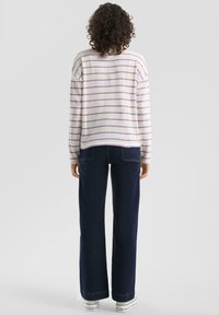 Sweter w białe i fioletowe paski, o luźnym kroju, ze spuszczonymi ramionami. W połączeniu z ciemnoniebieskimi, szerokimi jeansami i białymi trampkami.