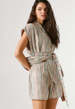 Naine kannab varrukateta triibulist vöös topi ja sobivaid lühikesi pükse, millel on pitsist lillemustriga tikand, seisab käed selja taga.