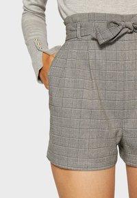 Pantaloni corti a quadri grigi con vita alta, dotati di una cintura da annodare, pieghe e tasche laterali. Realizzati in tessuto intrecciato con una finitura testurizzata.