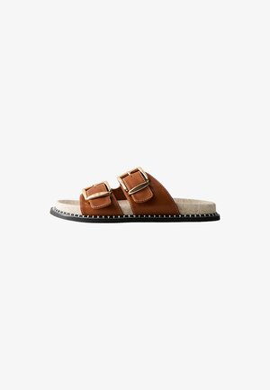 Bruine faux lederen slide sandaal met twee verstelbare gouden gespen, beige zachte voetbed en zwarte outsole met witte stiksel details.
