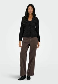 Blazer noir ajusté avec deux boutons, associé à un pantalon large marron et des bottines noires. Texture lisse, design ajusté, lignes épurées.
