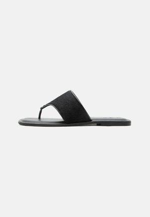 Sort flat slidesandal med bred teksturert stropp og tåstropp, vist mot en ensfarget lys bakgrunn.