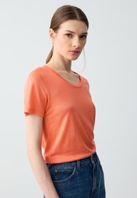 T-shirt a maniche corte e collo rotondo in morbido tessuto corallo, con una trama liscia e un fit rilassato, abbinato a jeans blu a vita alta.