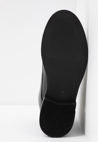 Suela de bota negra con goma texturizada, forma redondeada, tamaño 37 marcado. Borde superior liso con una ligera curva, detalles mínimos.