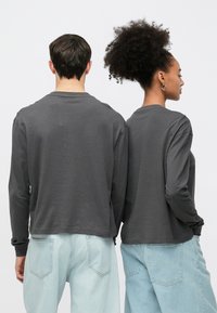 Gray long-sleeve shirts worn with light blue jeans, featuring a relaxed fit and round neck, displayed from the back.