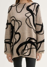 Kudottu beige villapaita, jossa on mustia abstrakteja, pörröisiä kuvioita. Ominaisuuksiin kuuluu pyöreä pääntie ja ribbaatut hihansuut. Rentoa istuvuutta, puolipitkä malli.