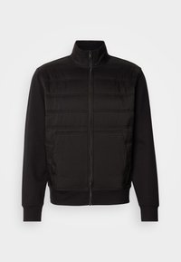 Veste noire zippée avec panneaux avant matelassés, col montant, poignets côtelés et poches latérales, présentée sur un fond blanc.