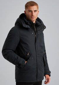 Črna izolirana jakna s kapuco, ki vključuje podrobnosti z zadrgo in pritisnimi gumbi, gladko teksturo in oprijet dizajn.