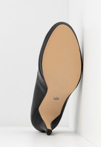 Chaussure à talon haut en cuir noir vue de la semelle, avec une semelle beige lisse et un petit bout de talon noir.