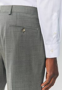Gray dress pants with a textured fabric, featuring a back pocket with a button closure. Accompanied by a white dress shirt with button cuffs.