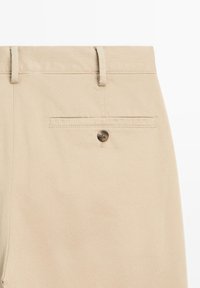 Beige cotton trousers featuring a rear patch pocket with a button closure, smooth texture, and standard belt loops at the waistband.