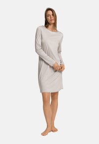 Světle šedá noční košile s dlouhým rukávem vyrobená z měkké látky, s kulatým výstřihem a uvolněným střihem, dosahující délky do poloviny stehen.
