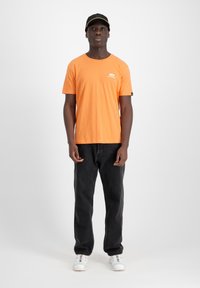 Tricou din bumbac portocaliu cu mâneci scurte, logo alb pe piept, asortat cu blugi negri și adidași albi; șapcă neagră cu accent portocaliu.