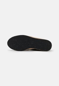 Semelle d'une chaussure noire avec motif antidérapant texturé et logo Calvin Klein Jeans embossé, présentée sur un fond blanc uni.