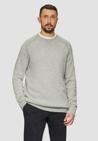 Jasnoszara dzianinowa bluza o teksturowym wykończeniu, z okrągłym dekoltem i ściągaczami przy mankietach. Noszona na czarnych spodniach. Prezentuje swobodny krój.