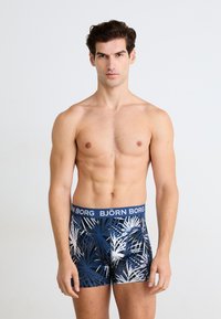 Herre boxershorts med en blå linning merket "BJÖRN BORG". Har et tropisk bladmønster i blått, hvitt og marineblått på en mørk bakgrunn.