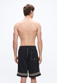 Μαύρο μαγιό σορτς με κίτρινες και γκρι λεπτομέρειες, �ελαστική μέση, μια πίσω τσέπη, ορατά ράμματα στο τελείωμα, σε προβολή από πίσω.