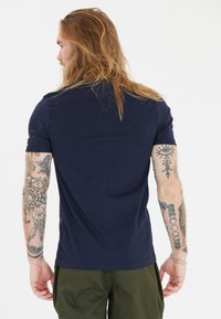 Marinblå kortärmad t-shirt i slät tyg, åtsittande design, med synliga tatueringar på armarna och en enfärgad rygg.
