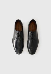 Black leather dress shoes with a smooth texture, pointed toe, and five lace holes. Inner lining is brown with "ALDO" printed.