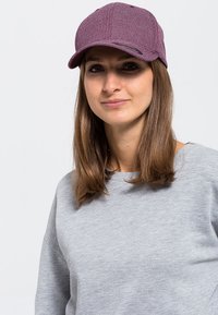 Mørk rosa caps med en teksturert overflate og buet skjerm, båret med en grå hettegenser som har en avslappet passform og rund hals.