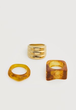 Három gyűrű fehér háttéren: egy fényes arany bordázott, egy borostyán áttetsző kerekített, egy borostyán áttetsző négyzet alakú.