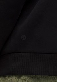 Schwarzer Stoff mit einem dezenten geprägten Lululemon-Logo über einem gerippten Saum und darunter grünen strukturierten Shorts.